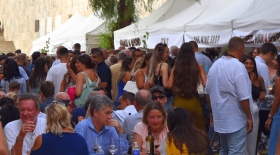 A lively outdoor wine festival in Gibraltar with many people gathered around white tents and tables, some sitting and enjoying wine, and others standing and socializing.